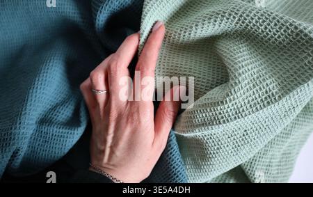 A hand reaches out to feel soft fabrics in two colors, mint green and blue. The focus is on the texture and the details of the woven materials. Settin Stock Photo