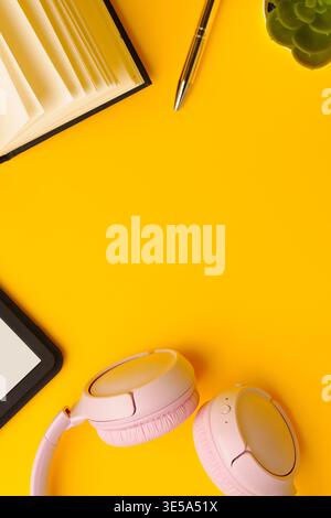 Relaxing workspace setup with headphones, a notebook, and a plant on a colorful yellow table Stock Photo