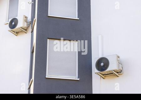 Outdoor unit of a split air conditioning system mounted on a white exterior wall Stock Photo