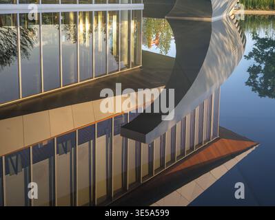A striking diagonal view of a modern building's sleek curved overhang and tall glass windows, creating a perfect symmetrical reflection in a dark, sti Stock Photo