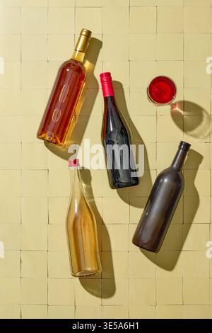 Top view of various wine bottles and wine glass arranged on a light sunny yellow background. Elegant composition with natural light and shadows, ideal Stock Photo