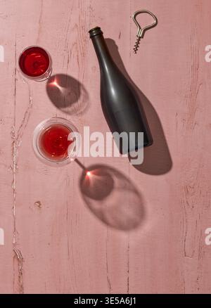 Top view of red wine in glasses with a dark bottle and corkscrew on a pink wooden surface. Stylish composition with sunlight and shadows, perfect for Stock Photo