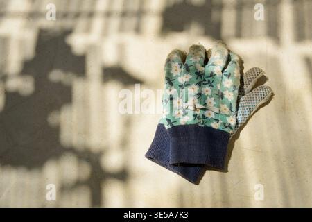 Old cotton gardening gloves with a floral pattern, lying on a table in the shade of the reed fences Stock Photo
