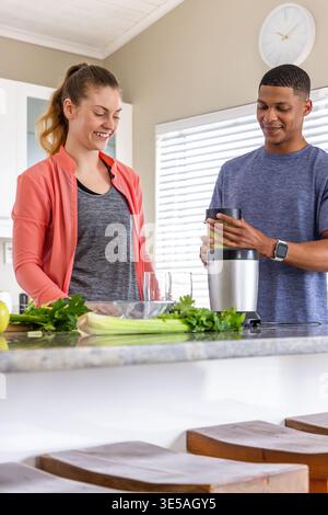 Couple with African American man in activewear preparing smoothie at home bar with blender, celery Stock Photo