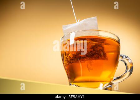 Glass cup of tea with tea bag inside on yellow background Stock Photo