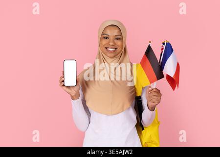 Black Muslim woman student in hijab holding blank smartphone and international flags Stock Photo