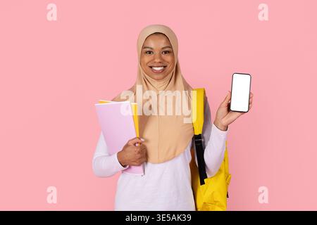 Black Muslim woman student in hijab holding blank screen smartphone and books Stock Photo
