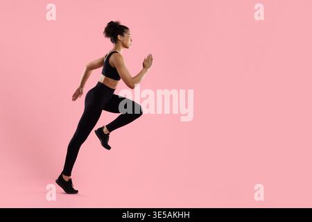Young sporty black woman running in place in activewear on pink background Stock Photo