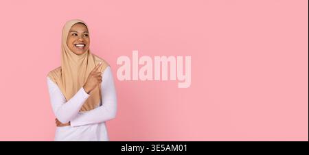 Young black Muslim woman in hijab pointing finger sideways while smiling Stock Photo