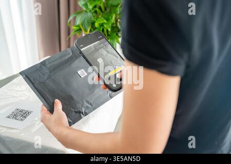 Person scanning QR code on parcel with smartphone camera with focus on mobile device screen. Digital app interface and contactless delivery service Stock Photo