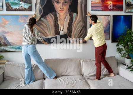 Creative married couple of painters hang painting on wall together in loft apartment workshop. Stock Photo