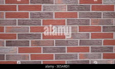 Brickwork made of multi-colored bricks with smooth seams and empty space on the textured surface, a wall made of gray, red and brown bricks Stock Photo