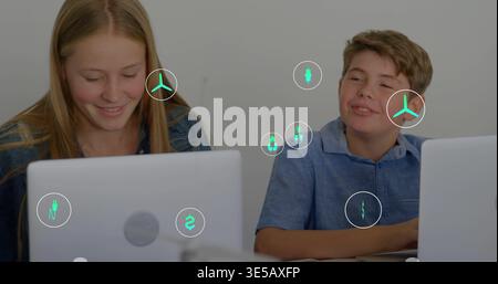 Smiling teens in denim jacket, blue shirt working in classroom with silver laptops and teal icons Stock Photo