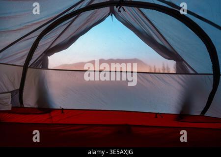 View from inside camping tent of foggy mountain and pine forest in tropical valley. Ideal for outdoor recreation and inspirational nature background Stock Photo