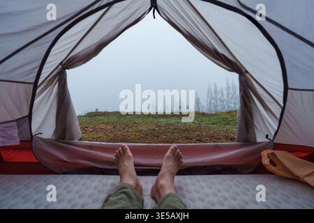 View from inside camping tent of foggy mountain and pine forest in tropical valley. Ideal for outdoor recreation and inspirational nature background Stock Photo