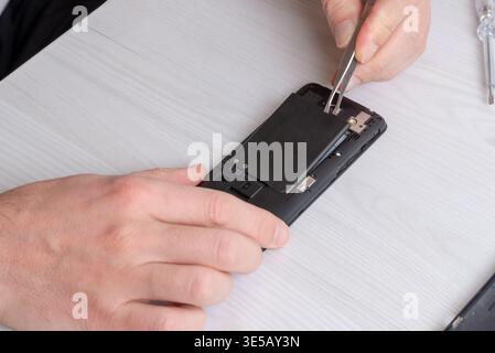 Close-up of technician installing smartphone battery using tweezers, focusing on precise placement and careful electronic repair workflow Stock Photo