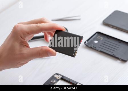 Hand holding smartphone battery above opened device, representing mobile repair concept, spare parts handling, and modern electronic servicing environ Stock Photo