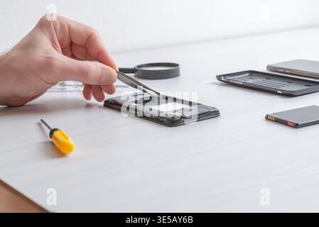 Tweezers adjusting internal smartphone connectors during repair, focusing on precision handling, delicate components, and electronic servicing workflo Stock Photo