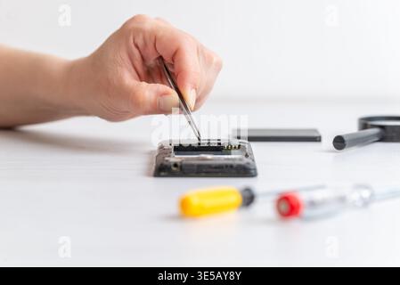 Tweezers placing small connector inside smartphone, representing precision electronics repair, delicate handling, and technical maintenance process Stock Photo