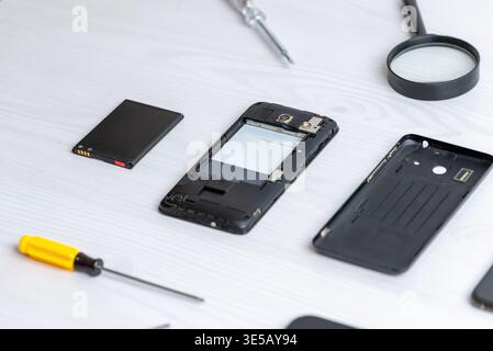 Disassembled smartphone with removed battery and tools on clean desk, illustrating mobile repair, maintenance process, and hardware inspection in mode Stock Photo