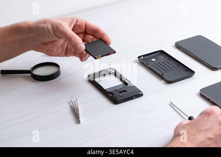Hand holding smartphone battery above opened phone during repair process, showing practical maintenance, replacement procedure, and electronic servici Stock Photo