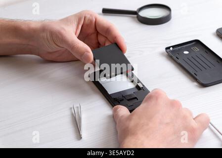 Close-up of smartphone battery being positioned inside device, focusing on precise repair action, component alignment, and mobile hardware servicing d Stock Photo