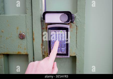 Person entering security code on electronic keypad access control system at metal gate with secure entry concept Stock Photo