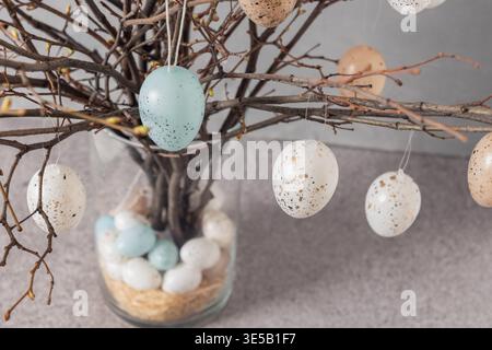Easter tree decorated colorful pastel white, blue and beige eggs. Birch branches with hang eggs in glass vase on gray table. Happy Easter greeting card. Close up Stock Photo