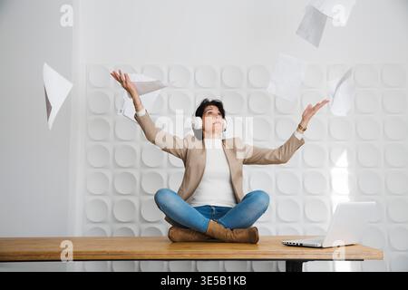 tired angry businesswoman touching head with laptop, she sits on a table and throwing up paper account documents Stock Photo
