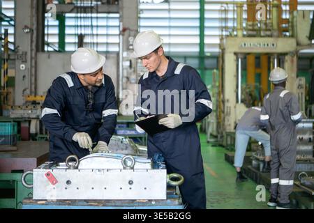 Industrial engineers and technicians discussing machine operation while inspecting equipment in a manufacturing factory Stock Photo