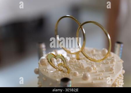 Elegant wedding cake with rings and white flowers, held by newlyweds in celebration. Stock Photo