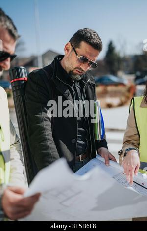 Architect and engineers reviewing blueprints on a construction site during an outdoor project meeting Stock Photo