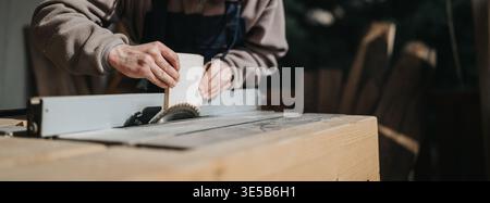 Craftsman cutting wood on a table saw in a workshop using hand-guided technique Stock Photo