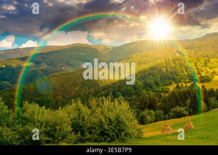 sunset over mountain hay field. alpine countryside summer landscape with green valley behind the woods on the grassy slope. cloudy sky. spectacular hi Stock Photo