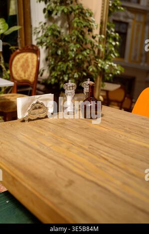 Spices, napkins, and an olive oil bottle on a rustic wooden cafe table. Detailed table accessories. Concept of high end catering and sophisticated din Stock Photo
