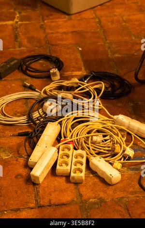 Electrical power strips and a mess of tangled cables create a tripping hazard on a brick floor Stock Photo