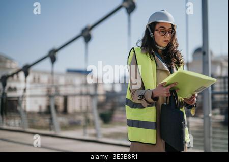 Female engineer inspecting urban construction site wearing hard hat and high visibility vest Stock Photo