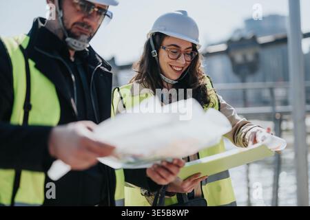 Construction engineers reviewing site plans on industrial work site wearing hard hats and safety vests Stock Photo