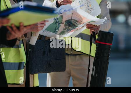 Construction engineers examining site plans and maps while wearing high-visibility safety vests Stock Photo