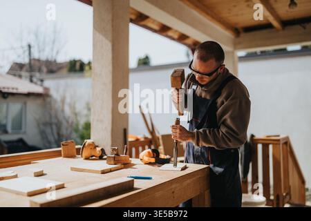 Carpenter working with chisel and mallet at a wooden workbench in a covered outdoor workshop Stock Photo
