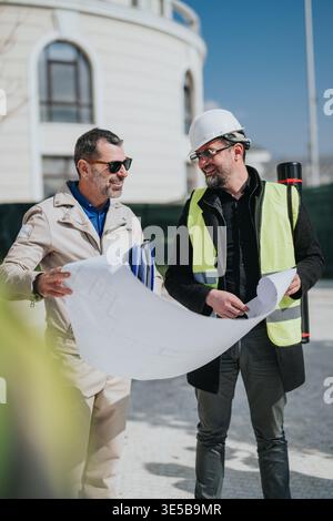Two construction professionals reviewing blueprints on site, architect and engineer discussing plans Stock Photo