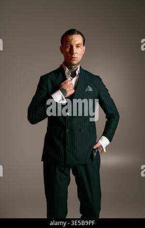 A stylish man adjusts his collar in a tailored suit against a simple background. Stock Photo