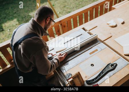 Carpenter cutting wood on a table saw in a bright outdoor workshop while wearing safety glasses Stock Photo