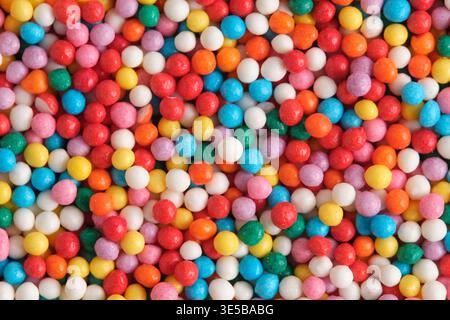 Top down view of round multi colored nonpareils sugar beads scattered evenly, featuring bright shades orange, blue, yellow, and pink Stock Photo