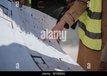Construction team reviewing blueprint plans on site with architect pointing at project layout Stock Photo