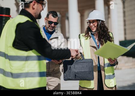 Construction engineers shaking hands on site with safety vests and hard hats, teamwork and agreement Stock Photo