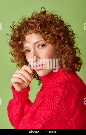 A young woman with red curls poses in a bright red sweater. Stock Photo