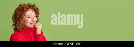 A cheerful young woman with stunning red curls showcases her happiness in a cozy sweater, banner Stock Photo
