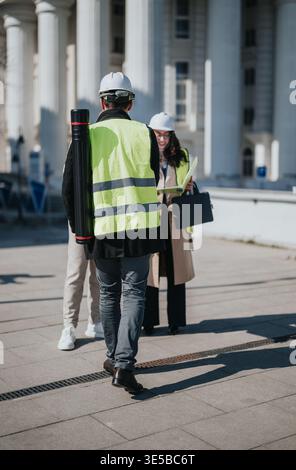 Construction professionals in high-visibility vests and hard hats reviewing plans outside a civic building Stock Photo