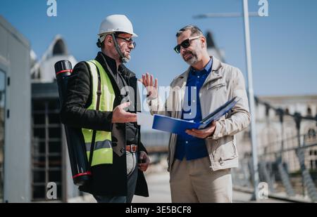Two architects discussing blueprints at a construction site during a project meeting Stock Photo